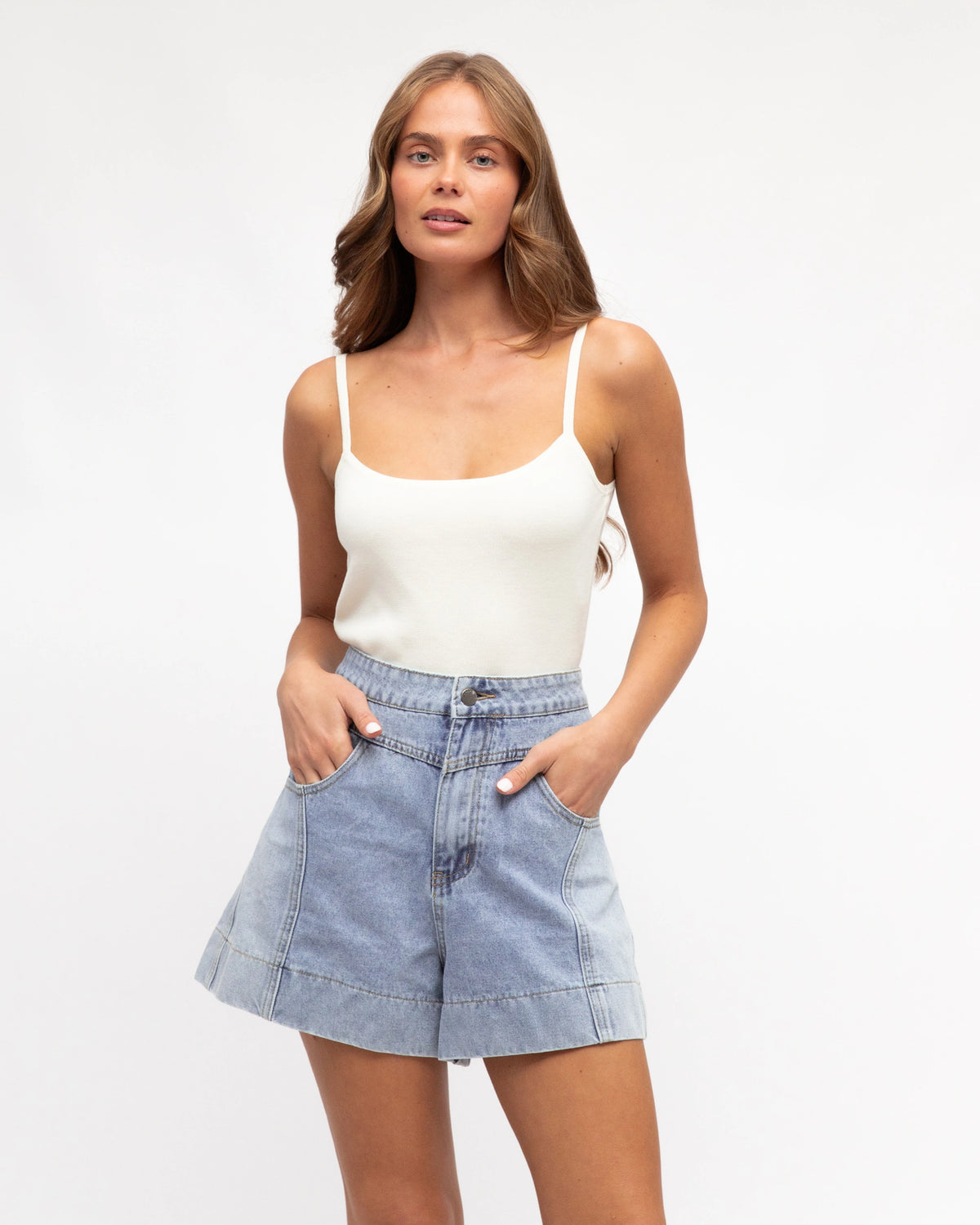 Woman wearing a white tank top and denim shorts on a plain background