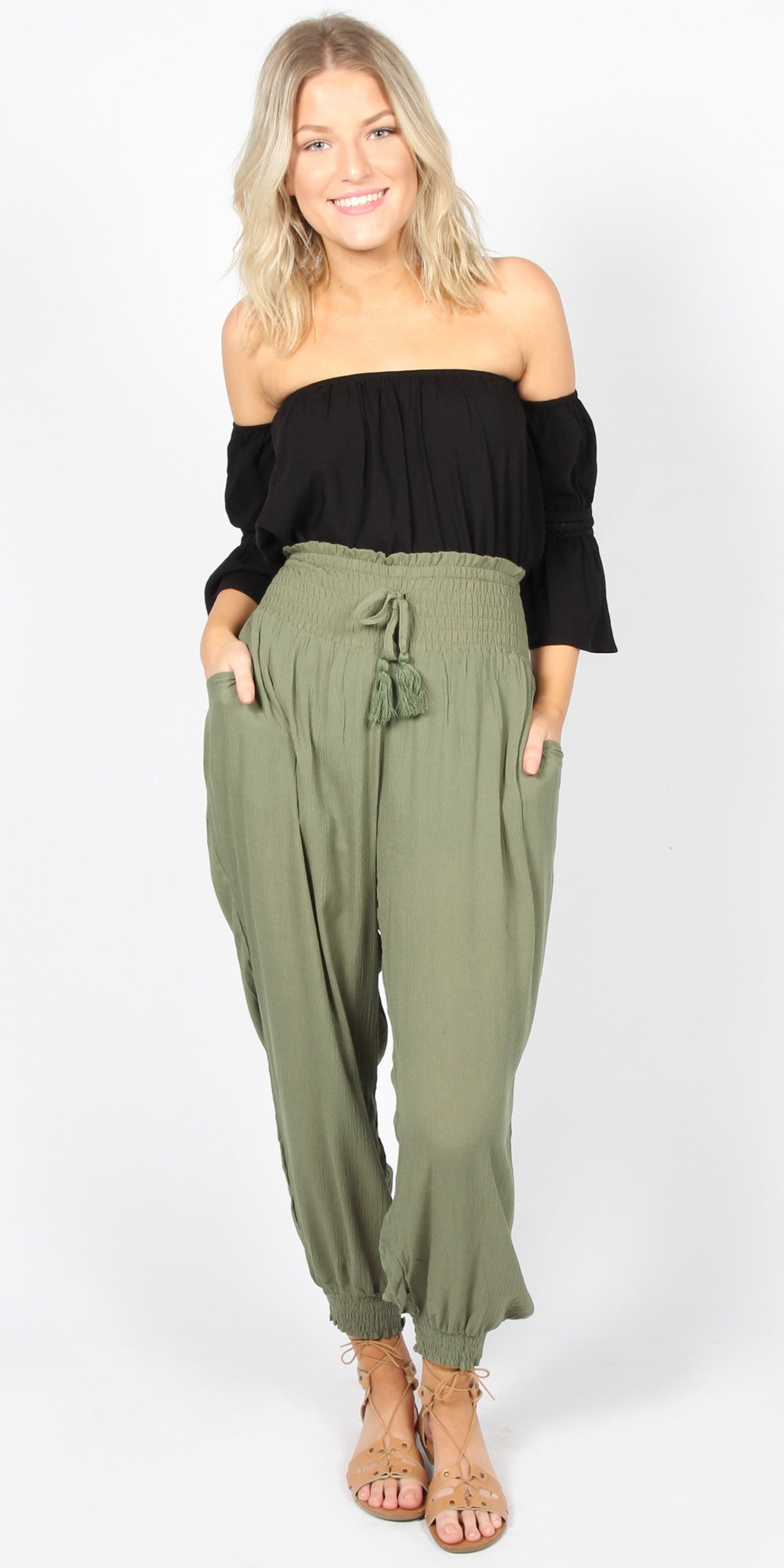 Woman wearing a black off-shoulder top and olive green jumpsuit on a white background