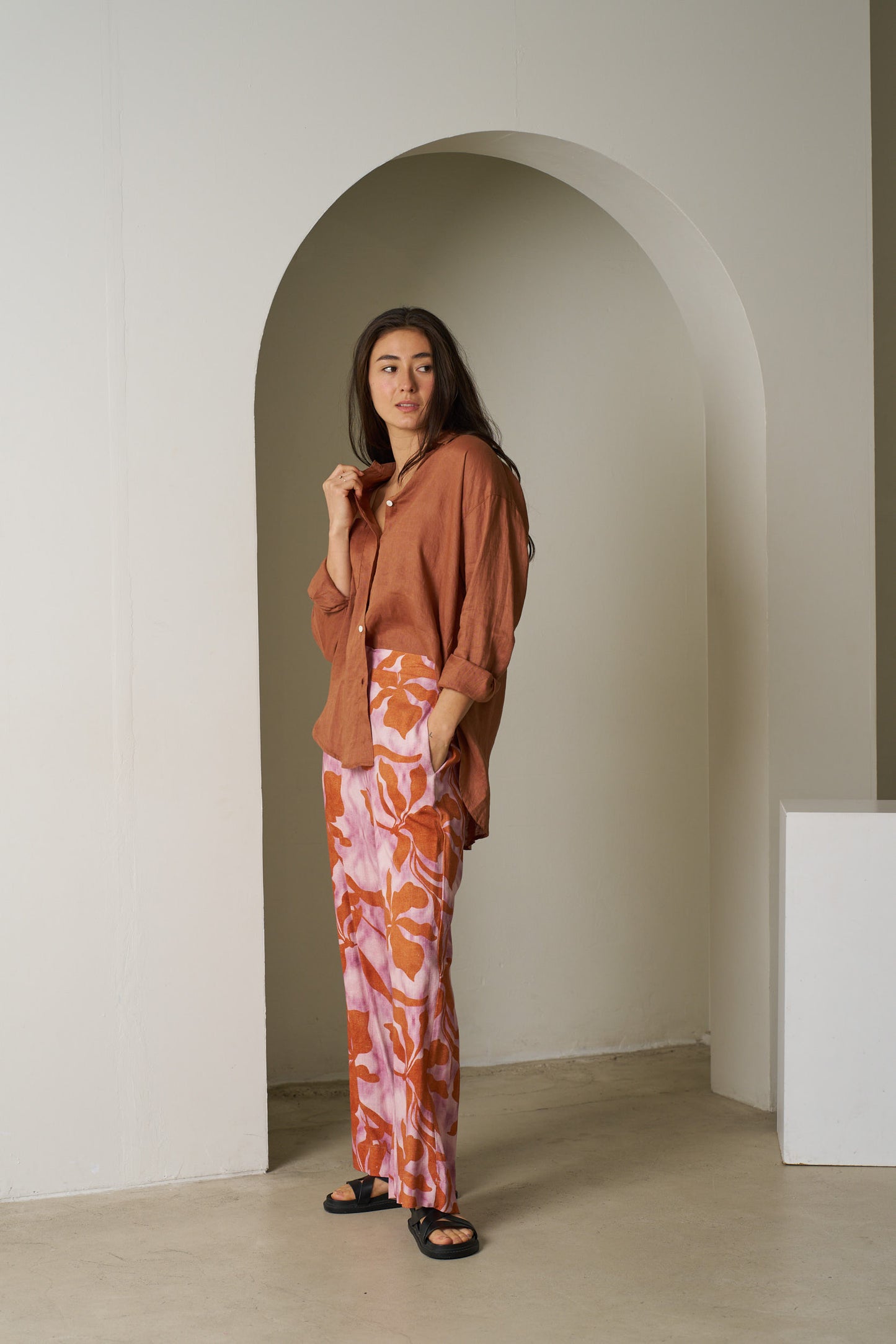 Woman in a rust-colored top and patterned pants standing in a minimalistic room with an archway.